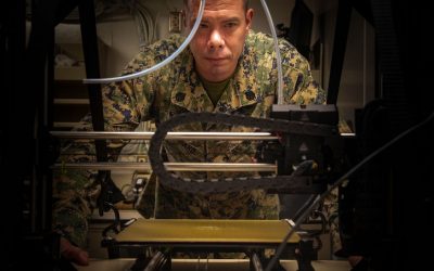 A U.S. Marine observes a 3D printer as it prints an equipment part used aboard USS New Orleans (LPD 18), Aug. 24.